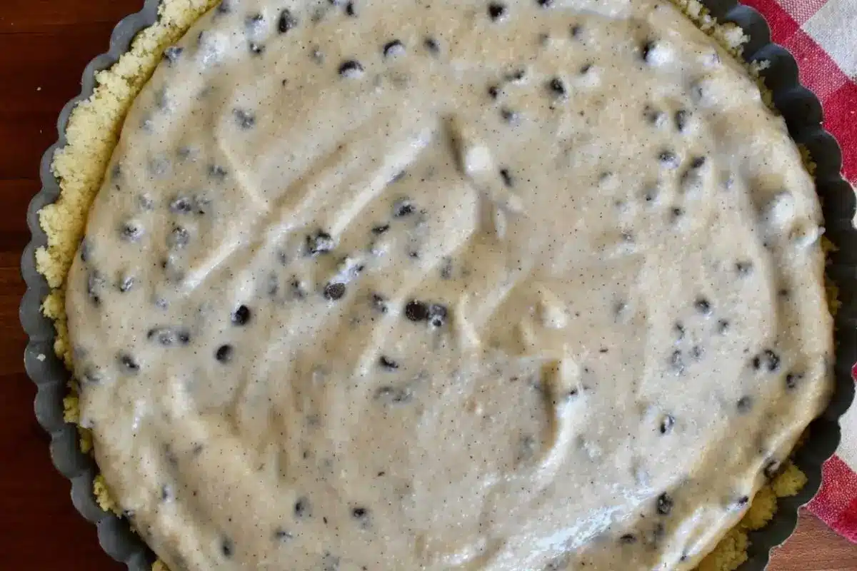 How to Make Ricotta Crostata Step-by-Step An overhead close-up showing a key step in how to make ricotta crostata, featuring a rustic fluted tart pan lined with buttery pastry and filled with a smooth, sweet ricotta and chocolate chip mixture.