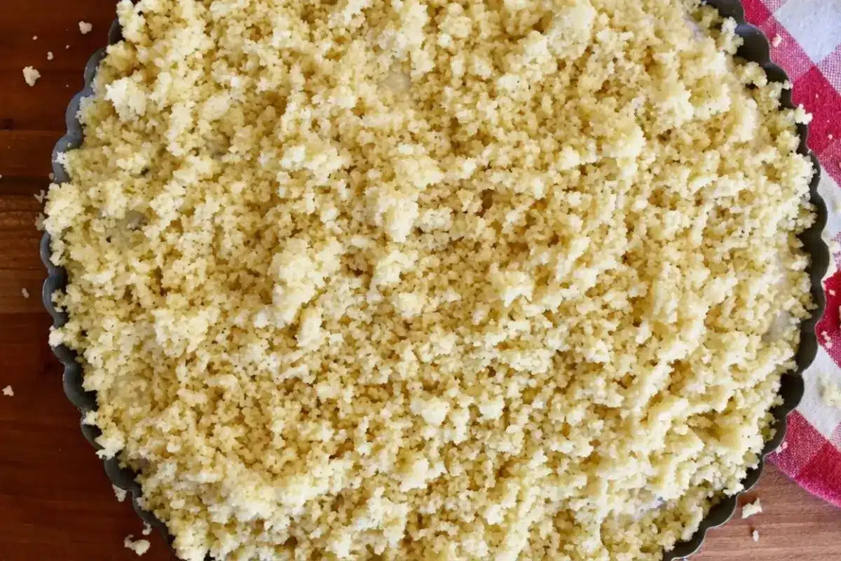 Rena's No-Fail Tips For Your Ricotta Crostata An overhead close-up showing a key step in how to make ricotta crostata, featuring a rustic fluted tart pan lined with buttery pastry and filled with a smooth, sweet ricotta and chocolate chip mixture.