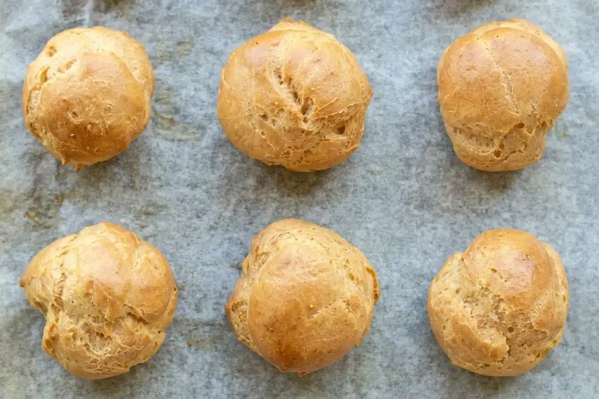 Rena's No-Fail Tips For your Italian Cream Puffs with Custard Filling Step-by-Step Six freshly baked, beautifully puffed and golden-brown pastry shells resting on parchment paper, showing the perfect, airy results of these no-fail Italian cream puffs.
