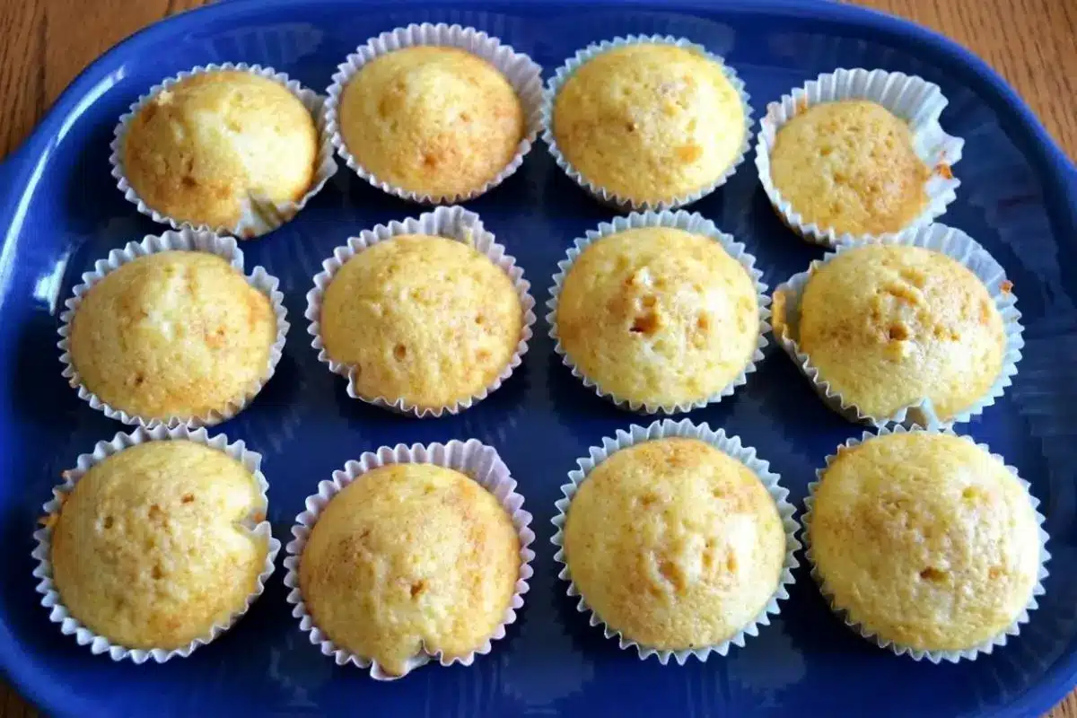 _Rena's No-Fail Tips for Your Tiramisu Cupcakes An overhead view of twelve freshly baked, golden unfrosted cupcakes in white paper liners resting on a deep blue platter, ready for the next step in making perfect tiramisu cupcakes.