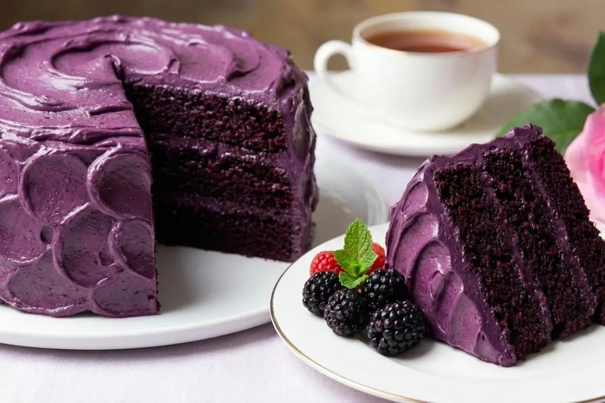 Storage & Freezing Dreamiest Blackberry Velvet Cake A sliced three-layer blackberry velvet cake with thick purple frosting sits on a white platter next to a single plated slice garnished with fresh berries, perfect for enjoying now or safely storing and freezing for later.