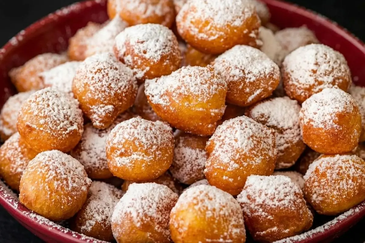 Storage & Freezing Pro-Tip for Busy Moms A close-up view of a rustic red bowl piled high with warm, golden fried dough generously dusted with powdered sugar, highlighting the best methods for freezing homemade zeppole.