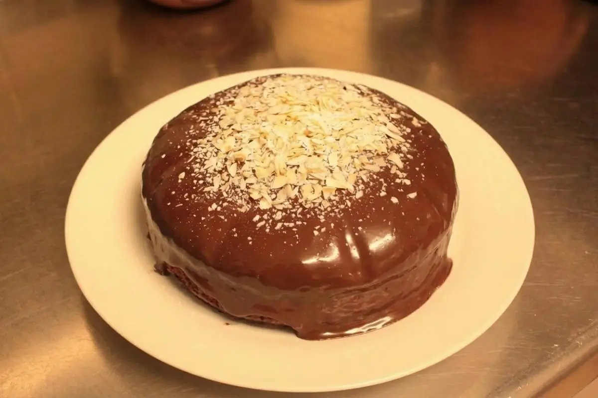 The Any Bowl Pan Prep & Make-Ahead Storage A deliciously glossy, chocolate-glazed Parrozzo cake topped with crushed almonds on a simple white plate, perfectly showcasing the beautiful results of our easy any bowl pan prep and make-ahead storage.