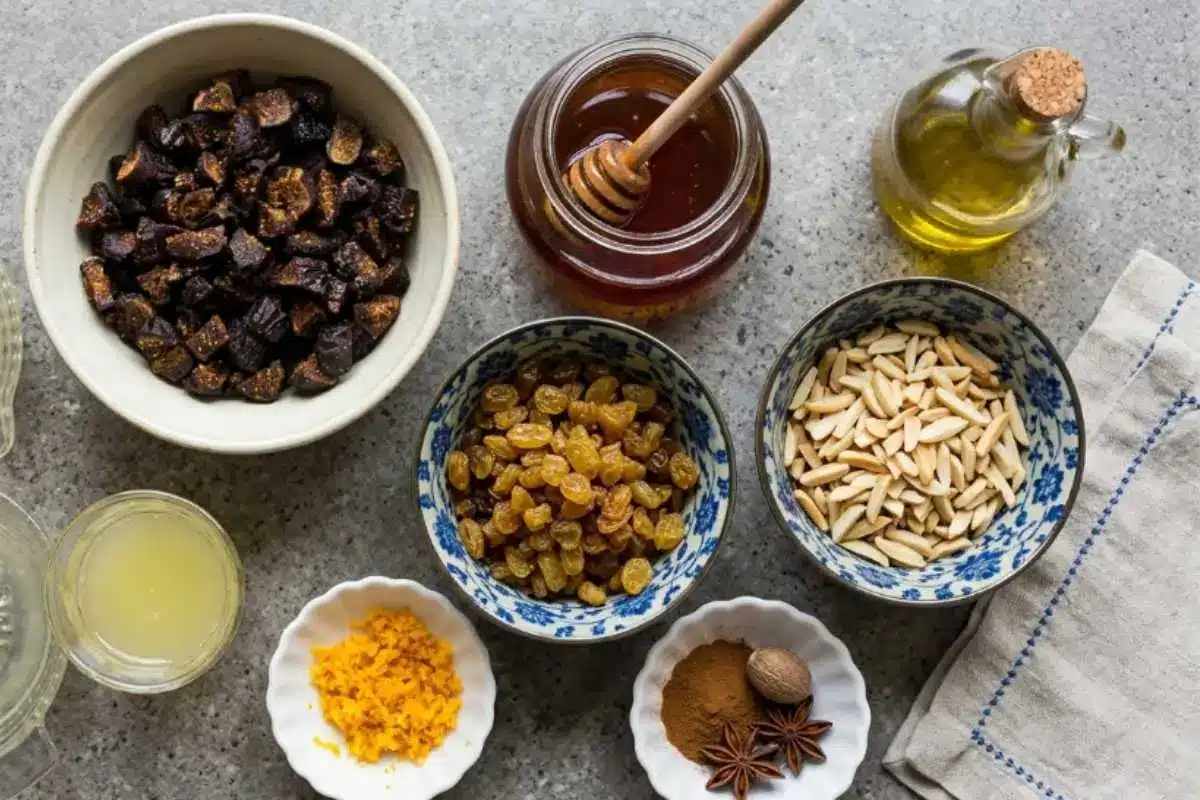 The Foolproof Ingredients & Heritage Variations An overhead view of traditional Italian fig cookie ingredients organized in small ceramic and glass bowls, featuring chopped dried figs, golden raisins, slivered almonds, honey, olive oil, citrus zest, and warm spices on a rustic stone surface.