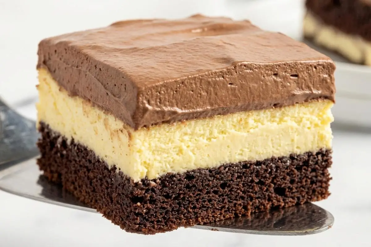 What Is Italian Love Cake A close-up of a freshly cut slice of Italian Love Cake resting on a silver serving spatula, revealing its three distinct layers of dense chocolate cake, creamy ricotta cheese filling, and rich chocolate frosting.