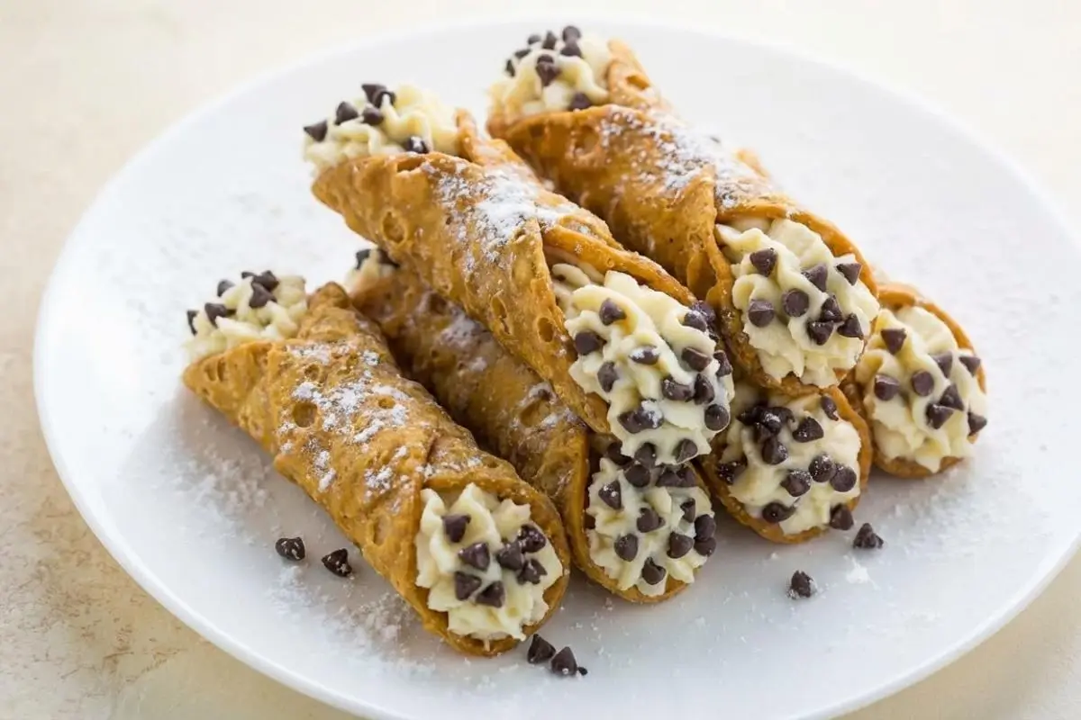Why This Cannoli with Ricotta and Chocolate Chips Works A white plate piled high with crispy, golden homemade cannoli with ricotta and chocolate chips, finished with a sweet dusting of powdered sugar.