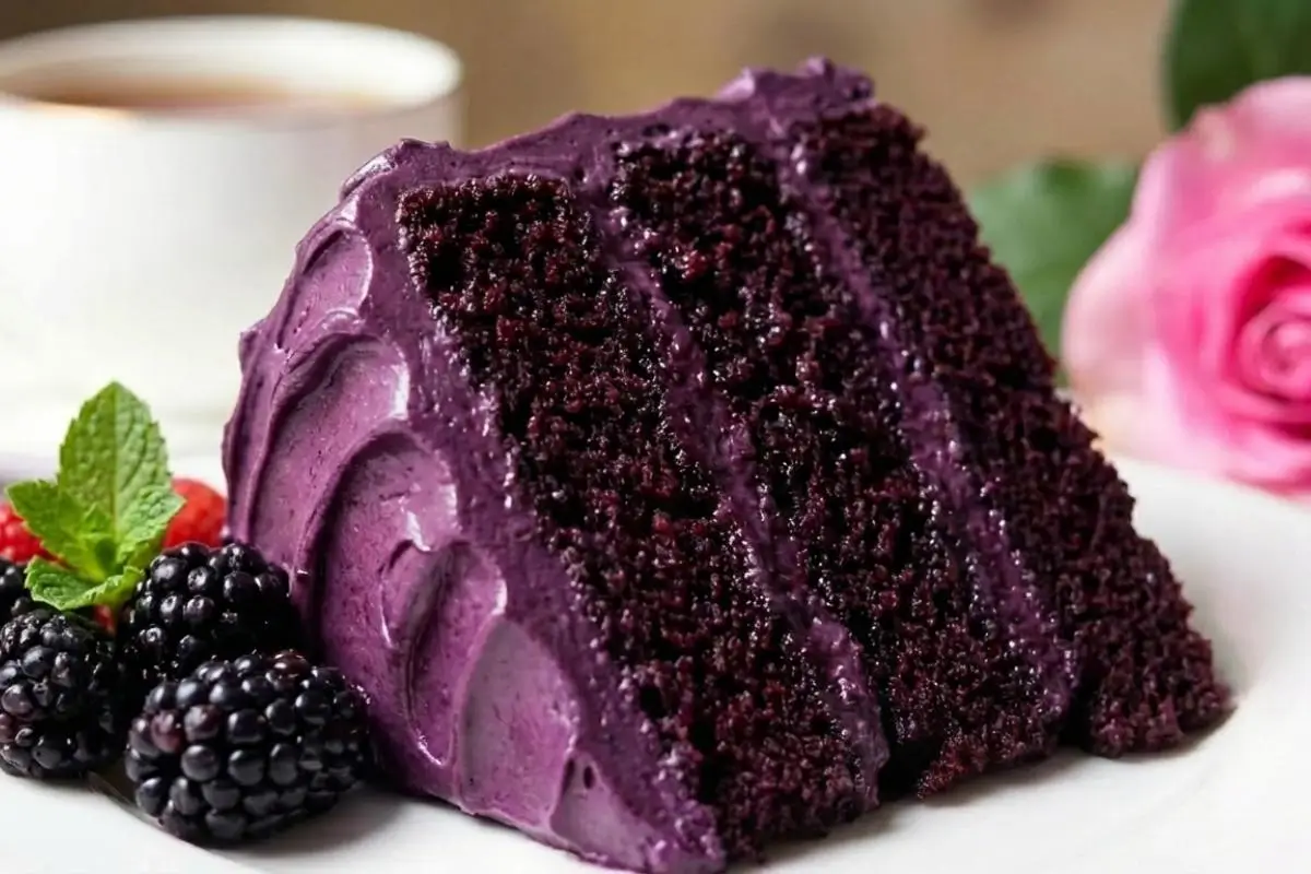 Why This Dreamiest Blackberry Velvet Cake Works A beautiful, thick slice of three-layer blackberry velvet cake with sweeping, glossy purple frosting, served on a classic white plate alongside fresh blackberries and a bright sprig of mint.