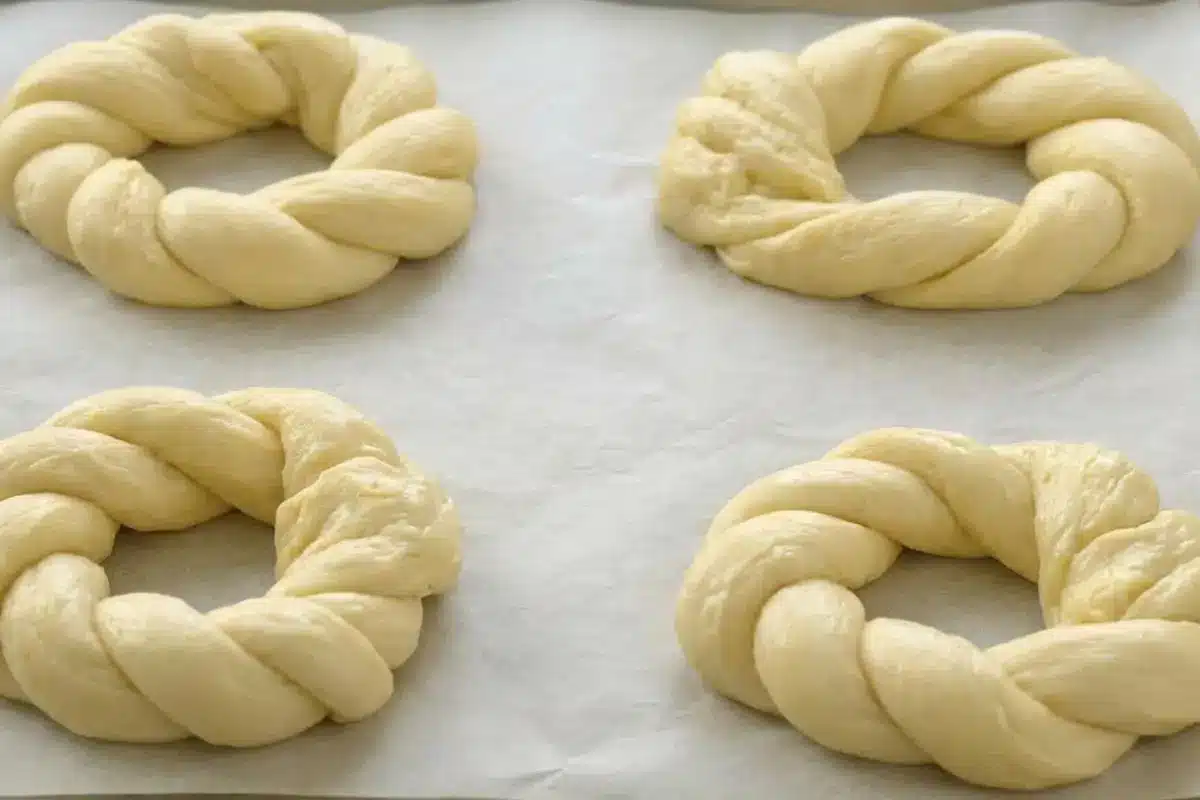 How to Make Italian Easter Bread Four braided raw dough rings resting on a parchment-lined baking sheet, demonstrating how to make Italian Easter bread just before it goes into the oven.