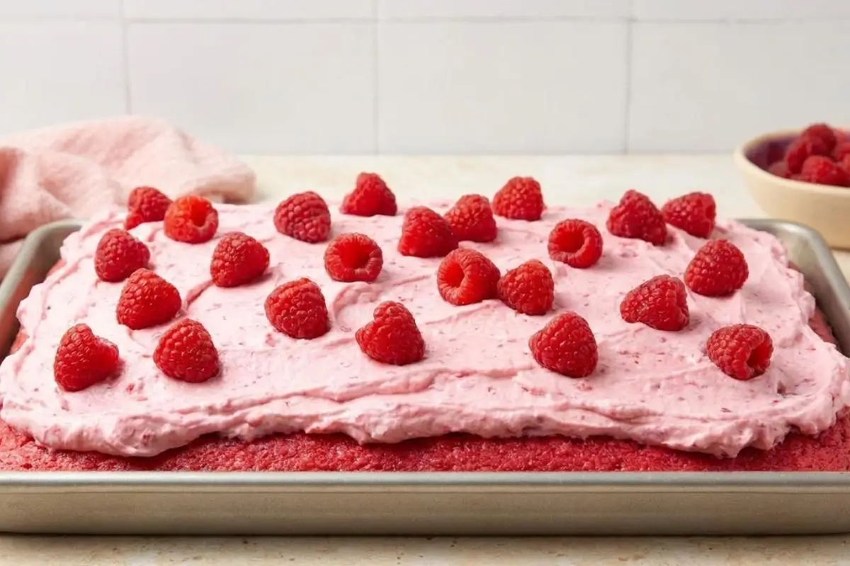 Serving and Storing Your Masterpiece For Raspberry Cake A freshly frosted pink raspberry sheet cake resting in a metal baking pan, generously topped with rustic swoops of pink frosting and scattered fresh raspberries, ready for serving and storing.