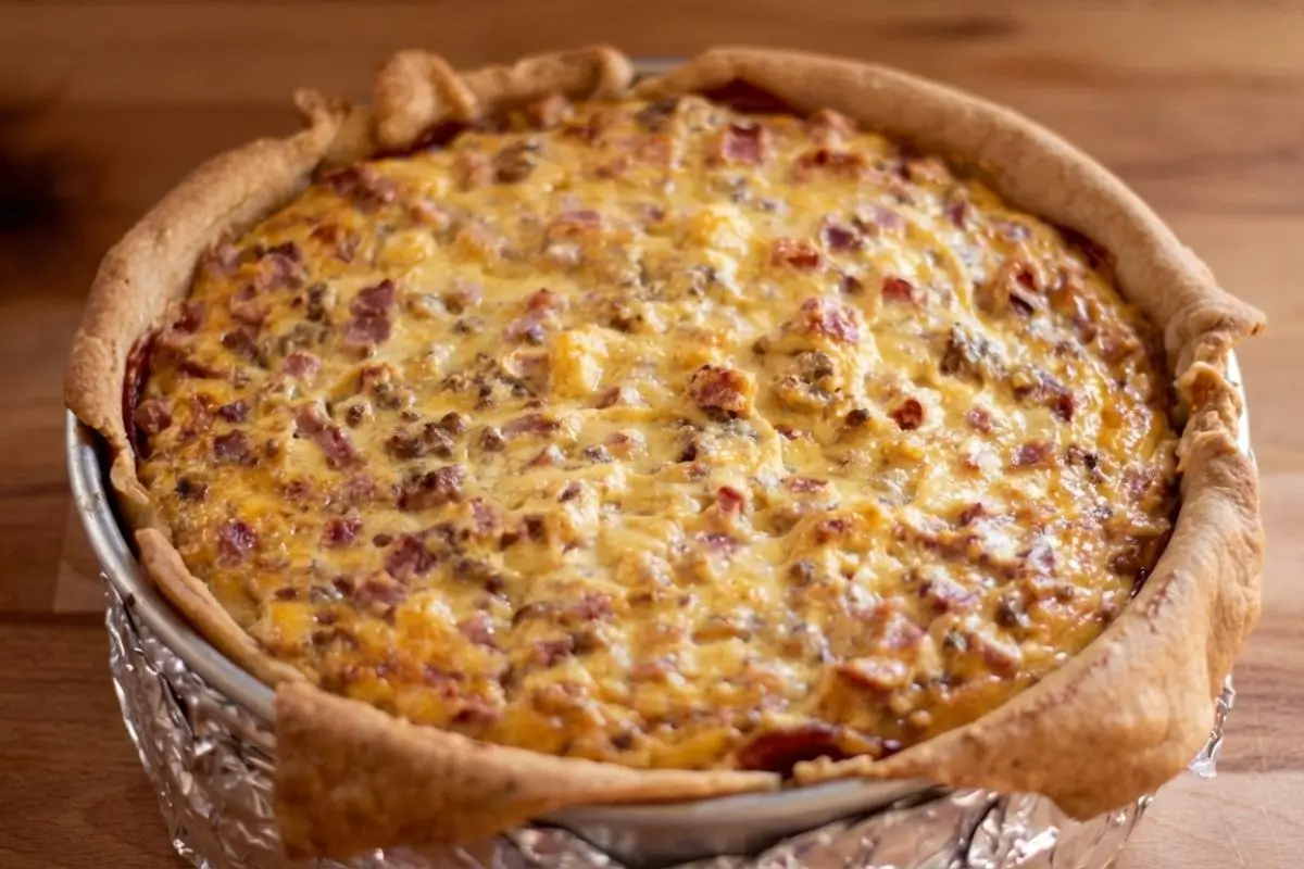 The Foolproof Ingredients List For your Italian Easter Pie A freshly baked Italian Easter Pie with a folded rustic crust, showcasing a rich, golden filling of diced meats and cheeses inside a foil-wrapped pan on a warm wooden table.