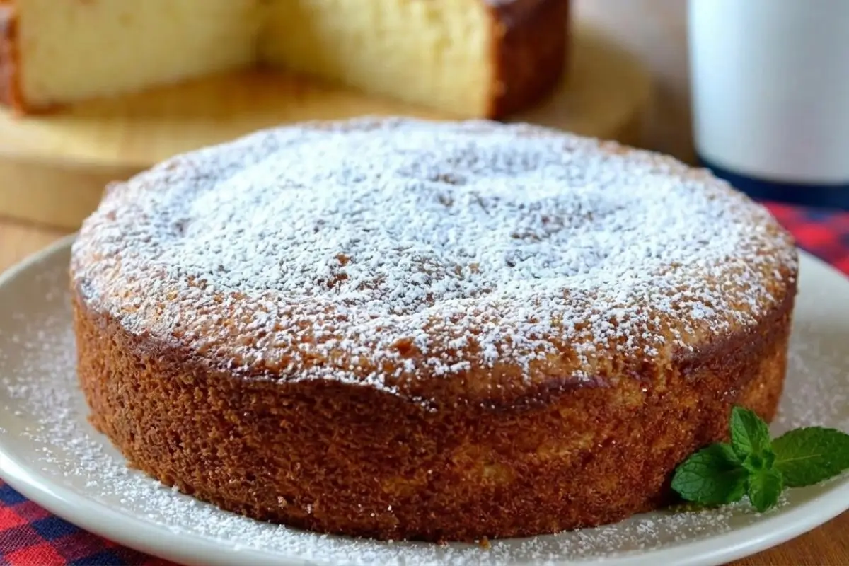 Why This Italian Lemon Ricotta Cake Works A whole, rustic Italian lemon ricotta cake with a golden-brown baked edge, generously dusted with powdered sugar and resting on a simple ceramic plate.