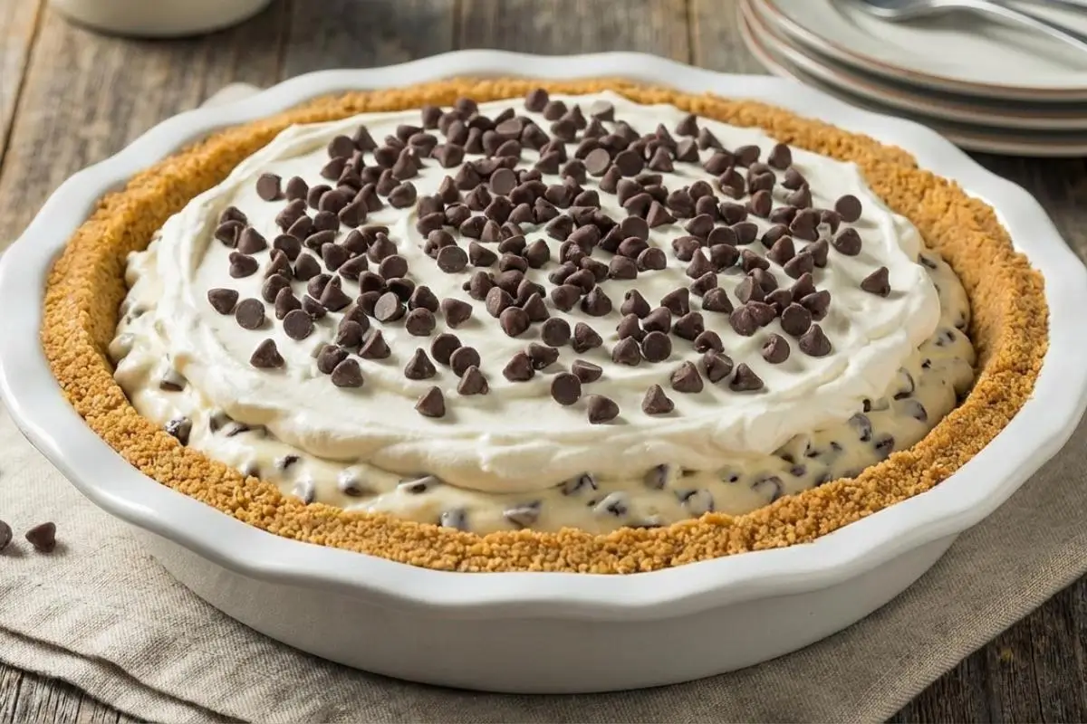 Why This Recipe Works Bakery Secret A beautifully layered chocolate chip cookie dough pie in a white ceramic dish, featuring a golden graham cracker crust, creamy filling, and fluffy whipped cream generously topped with mini chocolate chips on a rustic wooden table.