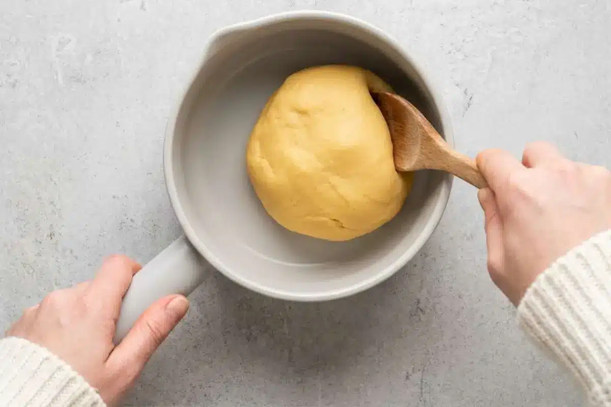 moms-famous-cream-puffs-recipe-choux-dough Smooth choux dough being stirred in a saucepan with a wooden spoon while making Mom’s famous cream puffs recipe.