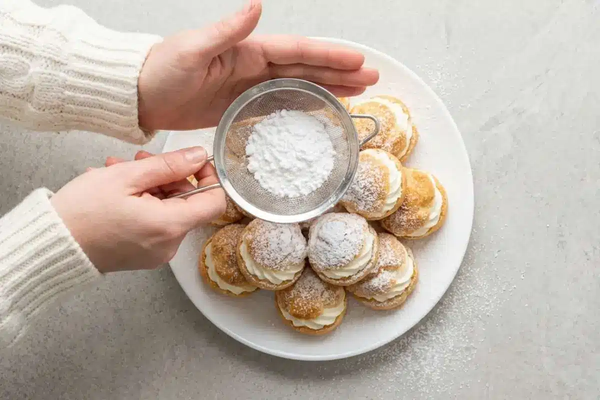 moms-famous-cream-puffs-recipe-powdered-sugar-finish Freshly filled cream puffs dusted with powdered sugar on a white plate for Mom’s famous cream puffs recipe.