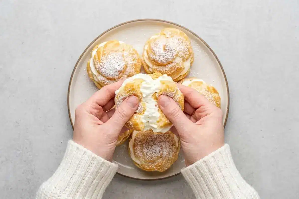 moms-famous-cream-puffs-recipe Hands pulling apart a freshly made cream puff filled with whipped cream from Mom’s famous cream puffs recipe.