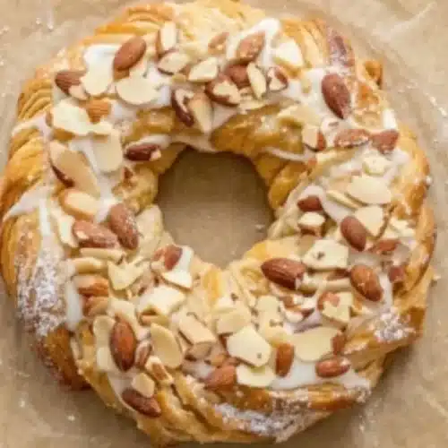 Flaky Homemade Almond Kringle: The Stress-Free Holiday Centerpiece Almond Kringle A golden, flaky Almond Kringle topped with sweet glaze, sliced almonds, and whole almonds, baked into a beautiful ring-shaped pastry.