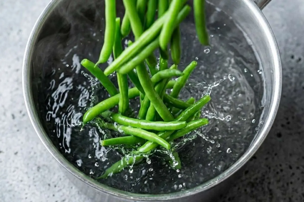 boiled-baby-potatoes-recipe-blanching-green-beans Fresh green beans being added to boiling water while preparing a boiled baby potatoes recipe with vegetables.