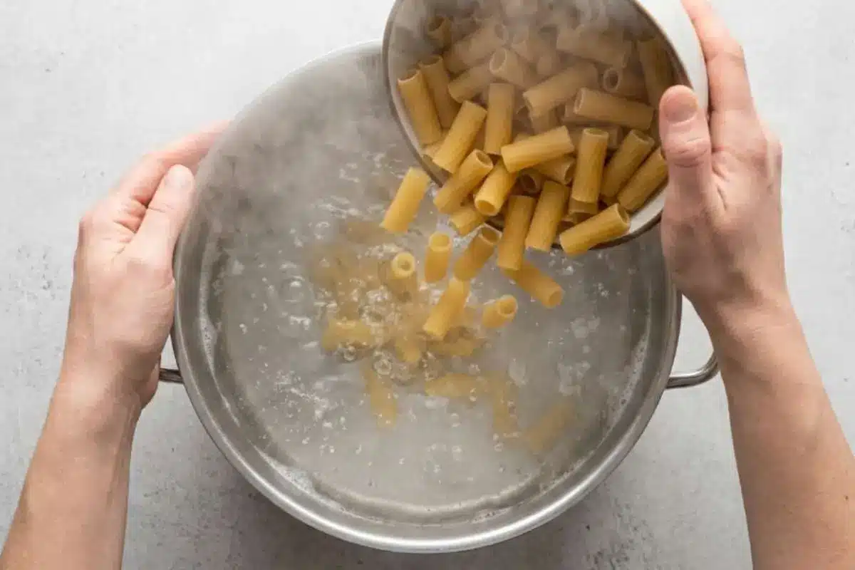 comforting-garlic-parmesan-pasta-boiling-rigatoni Rigatoni pasta being added to a pot of boiling water while preparing The Most Comforting Garlic Parmesan Pasta recipe.