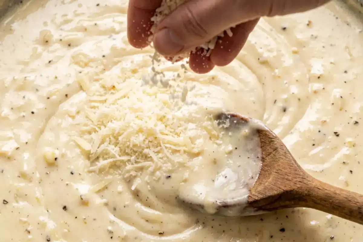 comforting-garlic-parmesan-pasta-parmesan-sauce Freshly grated Parmesan cheese being added to a creamy garlic sauce for The Most Comforting Garlic Parmesan Pasta recipe.