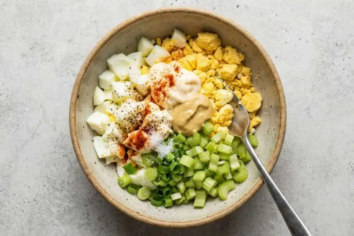 delicious-egg-salad-creamy-mixing-bowl (1) Hard-boiled eggs being chopped on a wooden cutting board for a Delicious Egg Salad recipe.