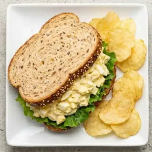 Delicious Egg Salad Recipe (Nonna’s Foolproof & Creamy Secret) egg salad recipe A homemade Delicious Egg Salad sandwich served on seeded bread with lettuce and potato chips on the side.