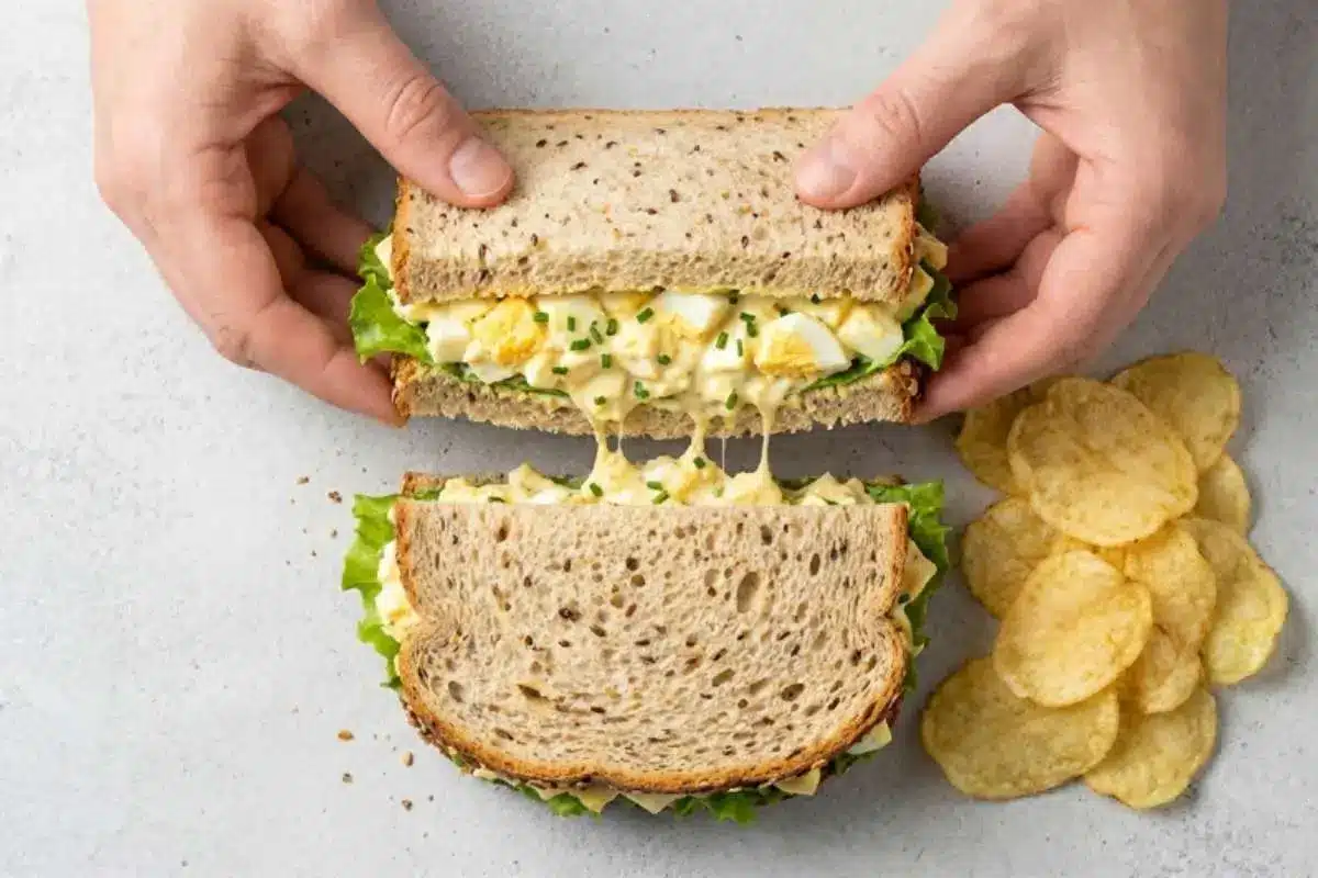 delicious-egg-salad-sandwich-with-chips A homemade Delicious Egg Salad sandwich on whole grain bread with lettuce and potato chips on the side, showing creamy egg salad filling.