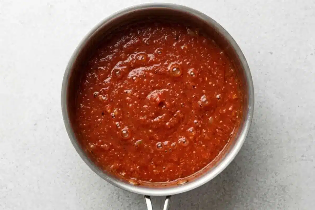 simmering-authentic-italian-sunday-sauce A pot of authentic Italian Sunday sauce gently simmering, with rich tomato sauce bubbling as the flavors develop during cooking.