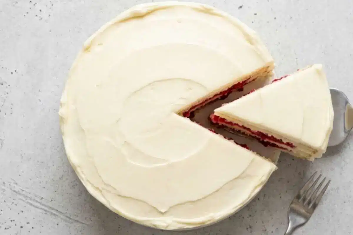 white-chocolate-raspberry-cake-recipe-slice A frosted white chocolate raspberry cake recipe with a slice removed, showing layers of raspberry filling and creamy white frosting.