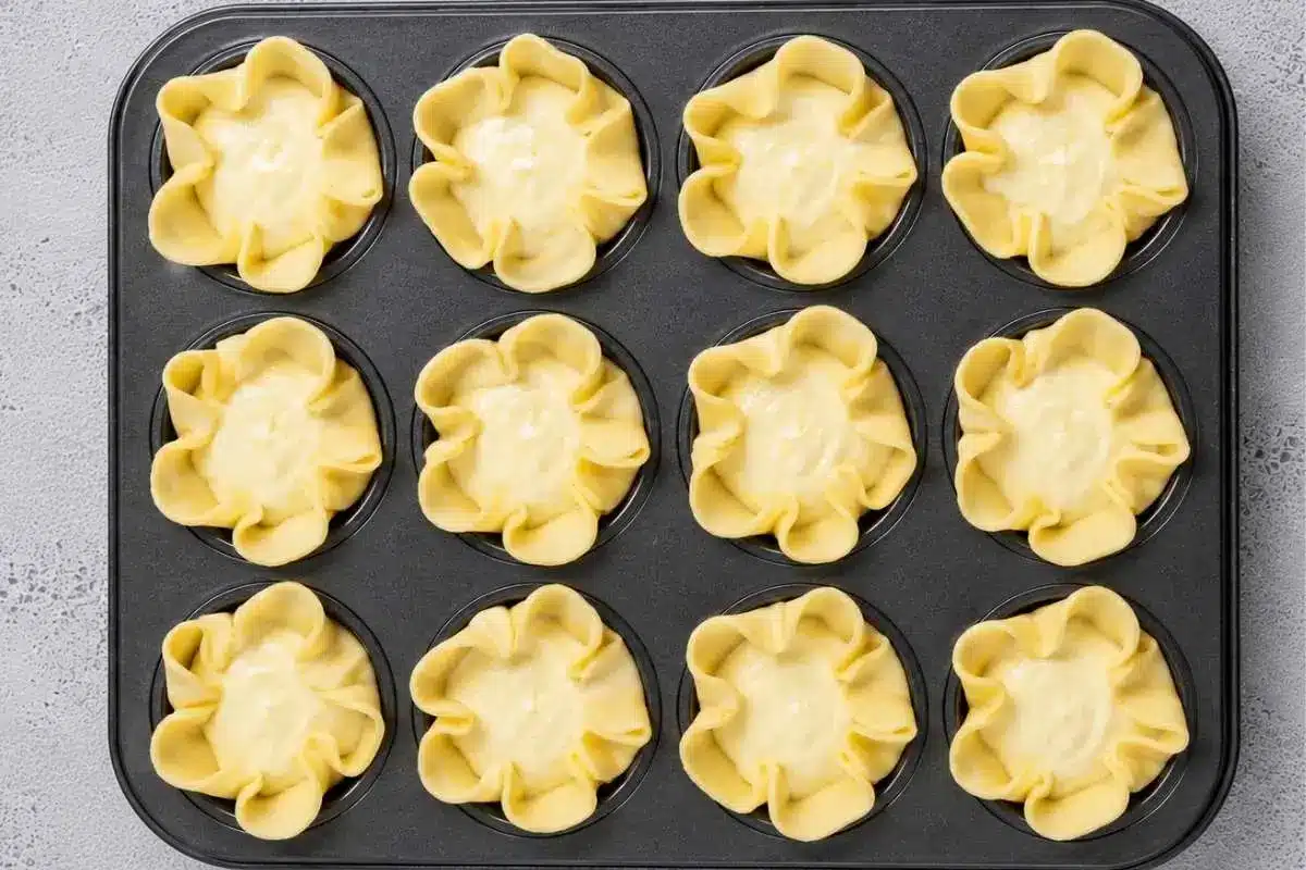 soffioni-abruzzesi-ready-for-baking Unbaked Soffioni Abruzzesi sweet ricotta pastries arranged in a muffin tin, with delicate flower-shaped pastry shells filled with creamy ricotta mixture and ready for the oven.